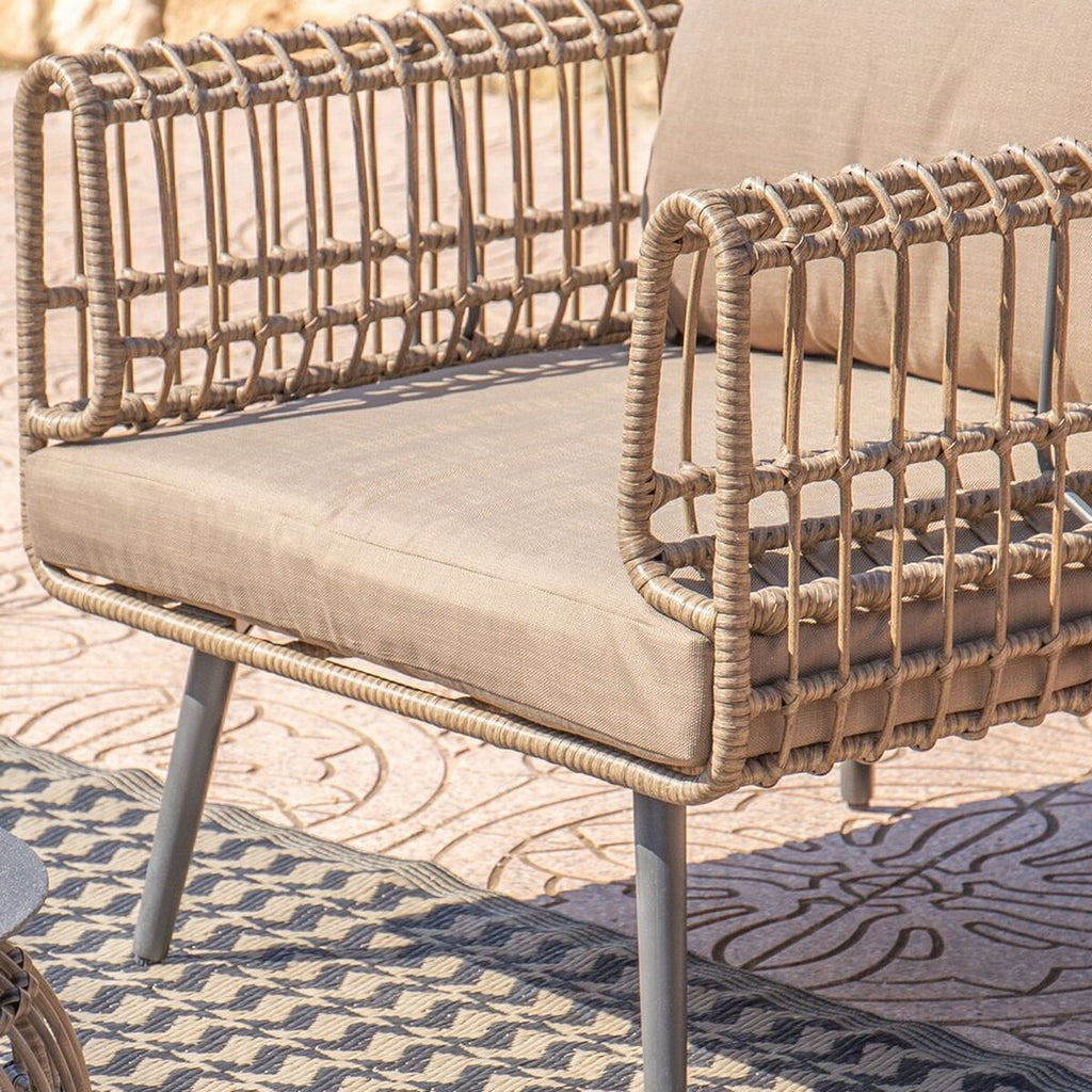 Side view of the 2-seater sofa showing detailed weaving of the synthetic rattan. The setting includes a sunny outdoor patio with a matching table.