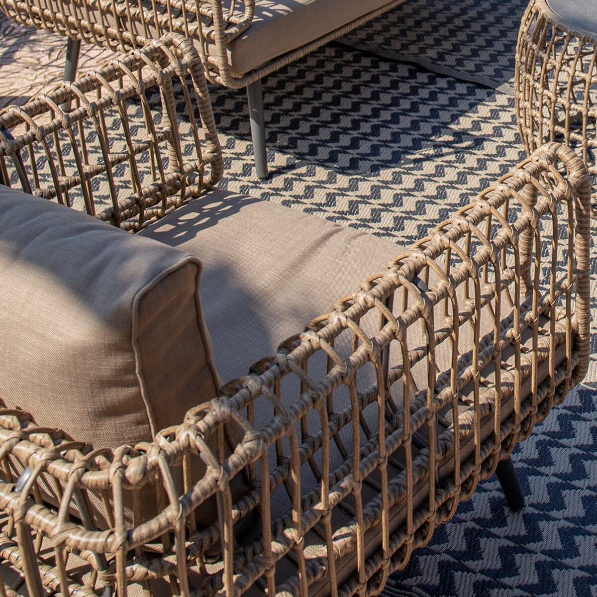 Close-up detail of the synthetic rattan weaving on the armrest of the 2-seater sofa, set against a patterned outdoor rug.