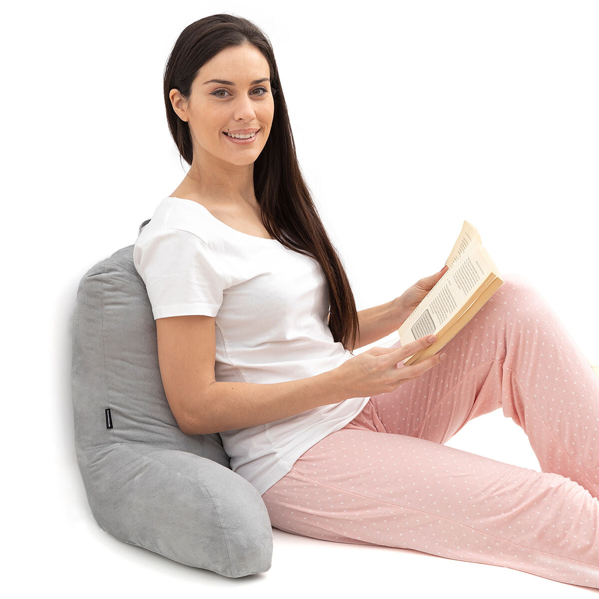 A woman leaning against the grey reading pillow while reading a book, highlighting its use for relaxation.