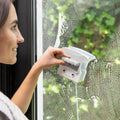 A person using the Magnetic Window Cleaner on a glass panel. The cleaner is being held with a firm grip, emphasizing its ergonomic design. The window has soap marks, suggesting active cleaning.