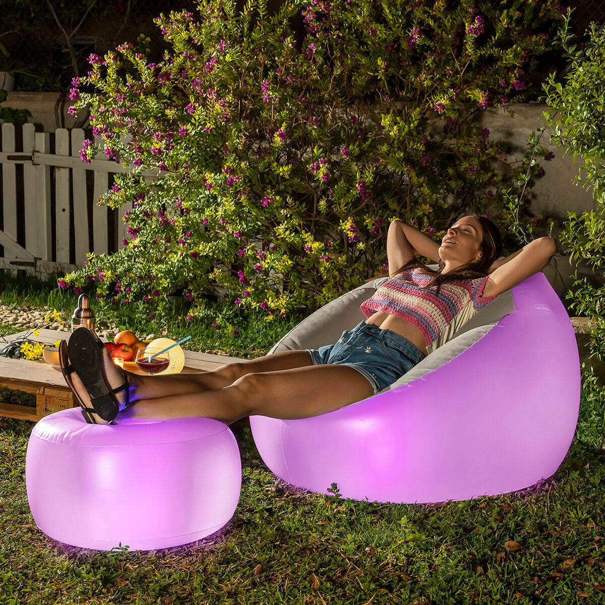 A woman relaxes outdoors on a purple-glowing chair, with her feet resting on a matching ottoman. This setting highlights leisure and casual luxury.