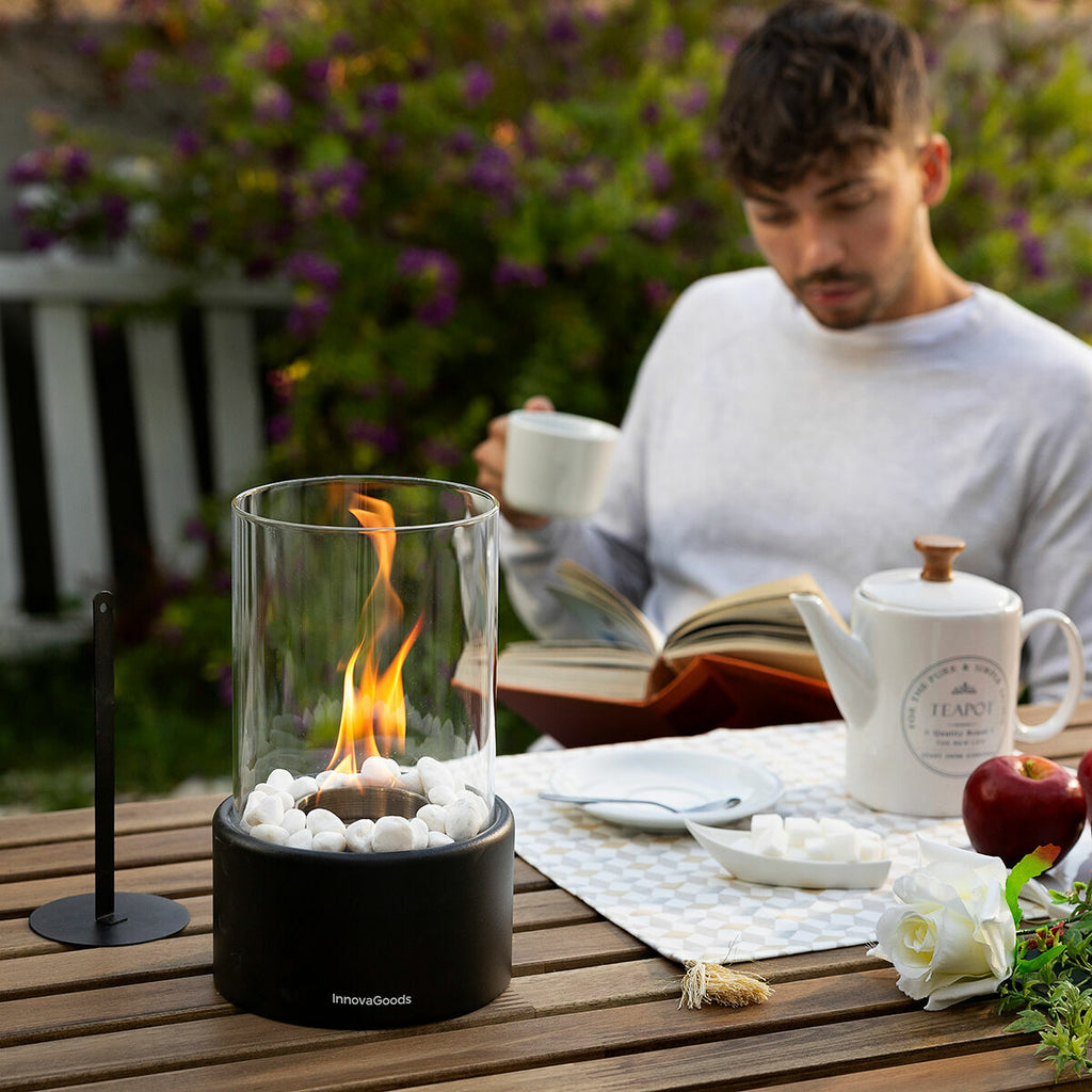 An outdoor setting with the fireplace on a wooden table next to a man reading a book and drinking tea, showcasing leisure time ambiance.