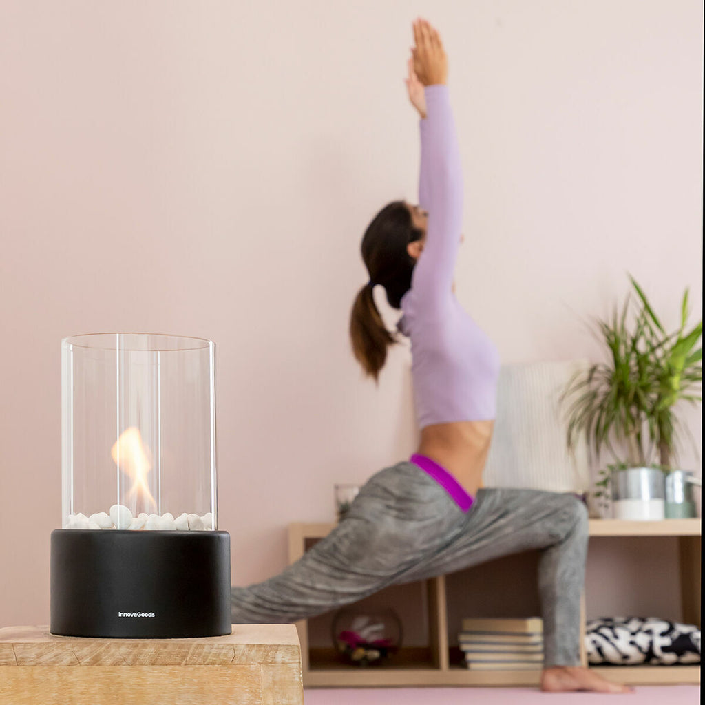 The fireplace is placed in a yoga room setting. A woman is performing a yoga pose in the background, presenting tranquility and relaxation.