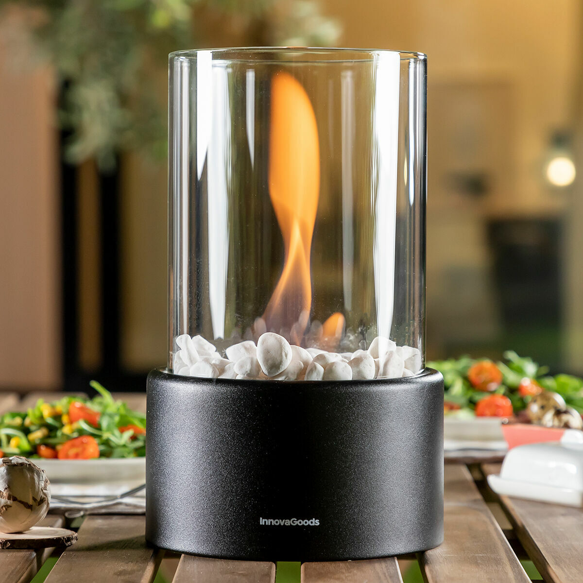 Close-up of the fireplace on a table with salad, highlighting the detailed design of the glass cylinder, flame, and decorative stones.