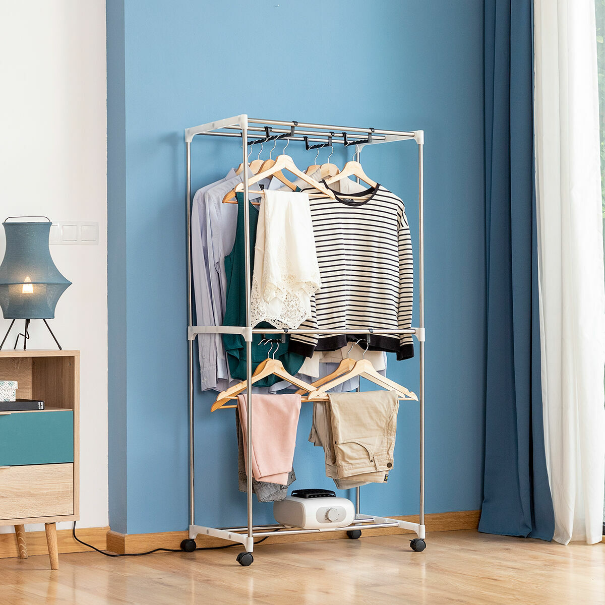 The assembled metal frame of the dryer with multiple clothes on hangers. The frame stands in a room with wooden flooring and blue walls, containing a lampstand and side table.