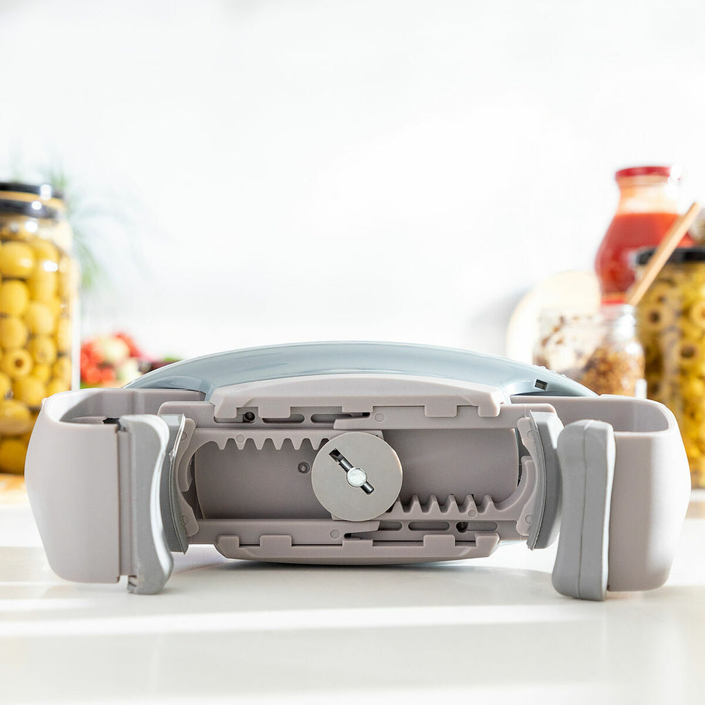 The underside of the Electric Jar Opener Lloucan InnovaGoods showing its gripping mechanism in detail. It is placed on a kitchen counter with jars visible in the background, suggesting its application context.