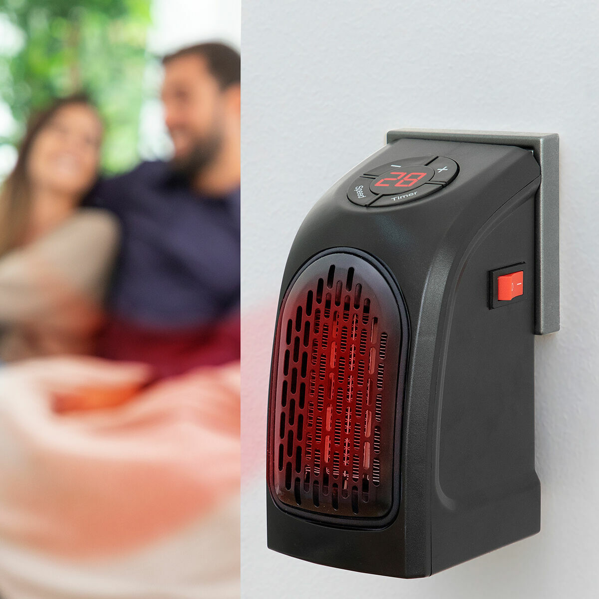 The heater is in use, plugged into a wall outlet. The adjoining blurred background shows a couple sitting comfortably, conveying warmth and ambiance.