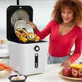 A woman is using the Ewooster electric composter in a kitchen setting, adding food waste from a bowl. The composter is white with a black control panel, featuring buttons and indicator lights.