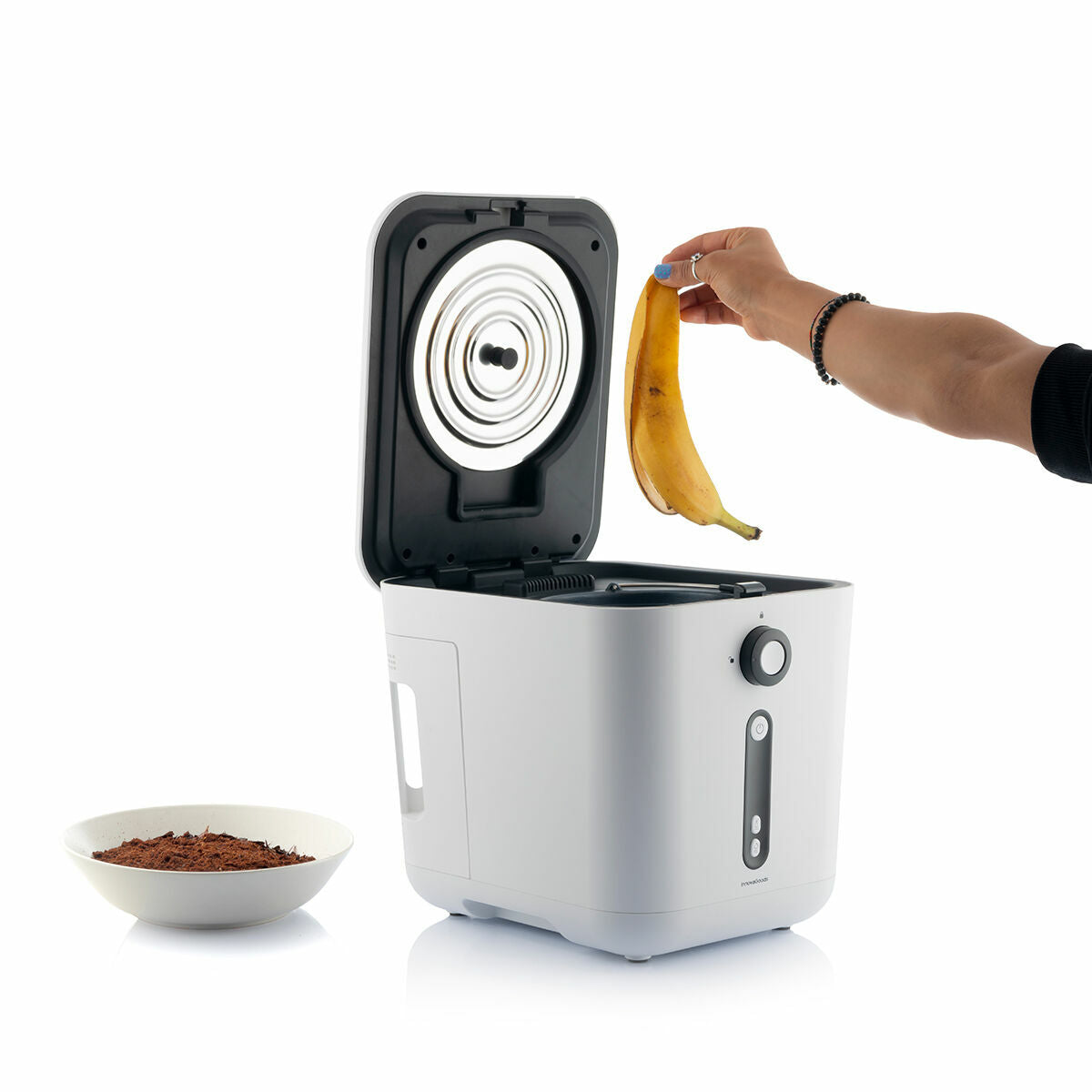 Demonstration of a hand placing a banana peel into the composter. A bowl of compostable material is nearby.