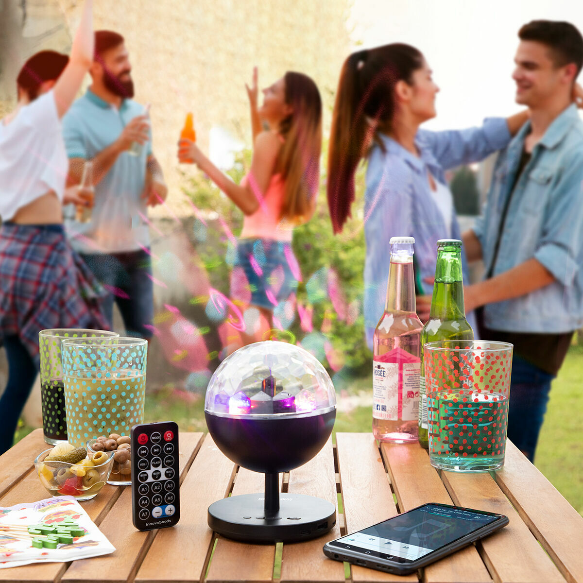 The projector on a table outdoors in a party setting, surrounded by drinks and snacks, indicating its role in enhancing outdoor gatherings with its light display.