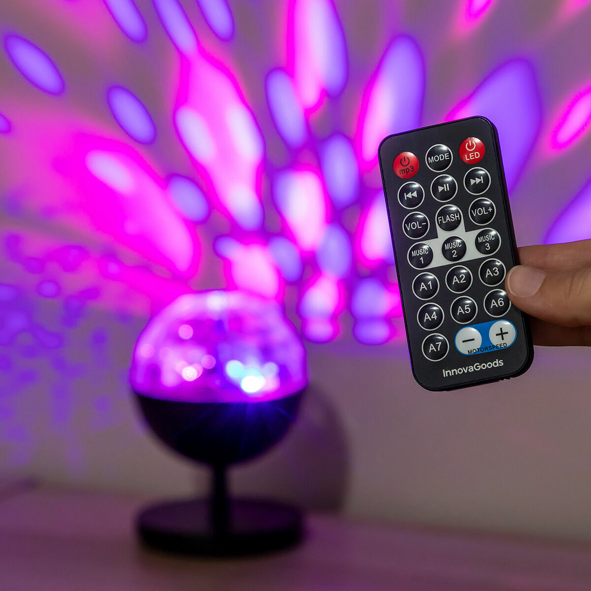 The image shows a person holding the remote control for the LED projector with an illuminating light display in the background, offering a close-up of the remote's features.