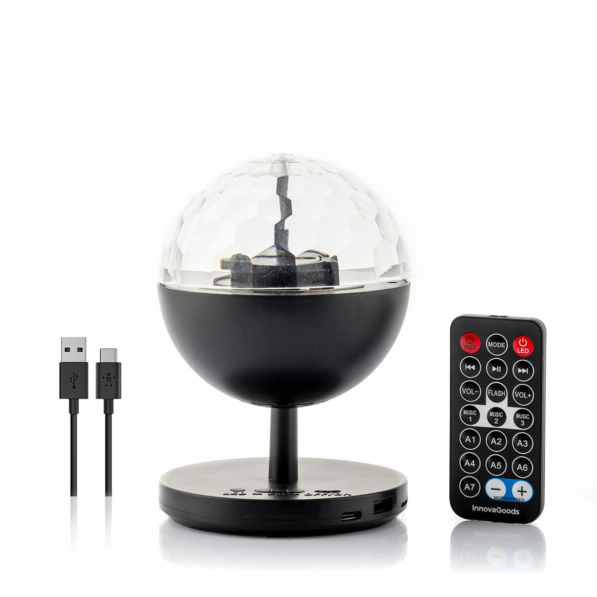 A detailed product shot showing the Rechargeable LED Projector with Speaker Istarlyt InnovaGoods along with its remote control and USB cables. The projector has a spherical design with a faceted dome.