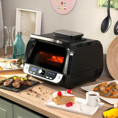 The air fryer is placed on a kitchen countertop, surrounded by prepared food such as steak, vegetables, and cake. The digital display is lit, showing 205°C.