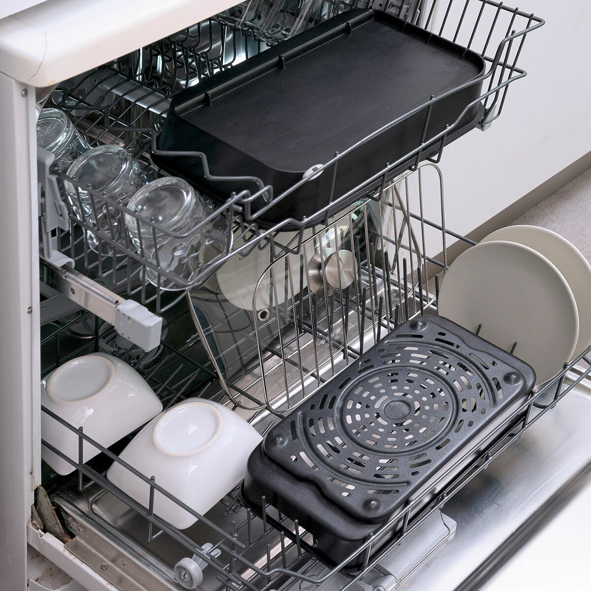 Dishwasher with trays and kitchenware inside, demonstrating the washability of accessories.