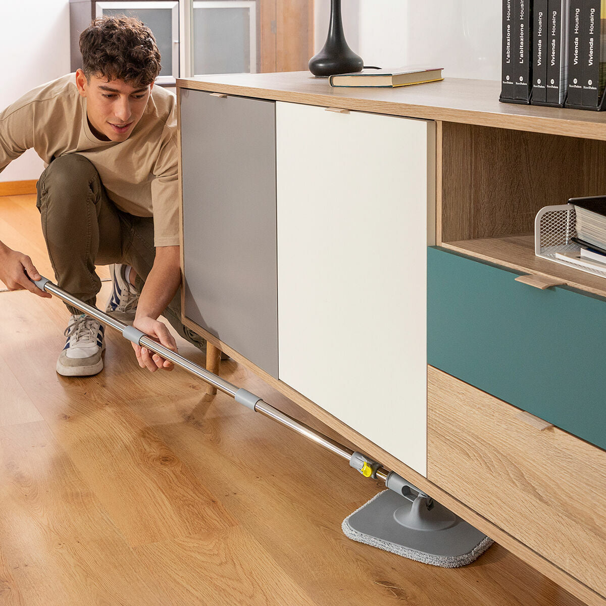 Person using the mop under furniture, highlighting flexibility and ease of use in tight spaces.