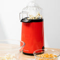 A red Hot Air Popcorn Maker Popmar InnovaGoods popping popcorn, with glass bowls on a wooden surface.