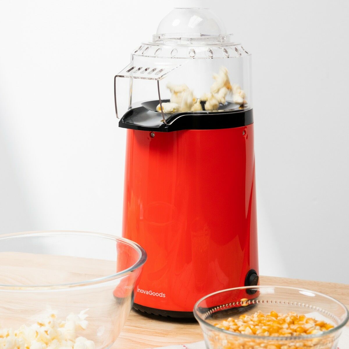 A red Hot Air Popcorn Maker Popmar InnovaGoods popping popcorn, with glass bowls on a wooden surface.