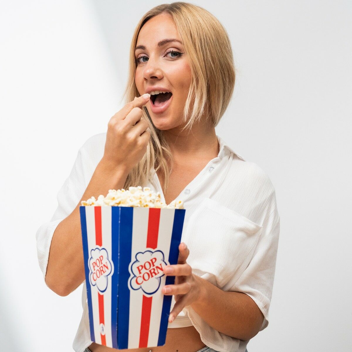 A person holding a popcorn bucket with branded 'Popcorn' label, appearing happy.