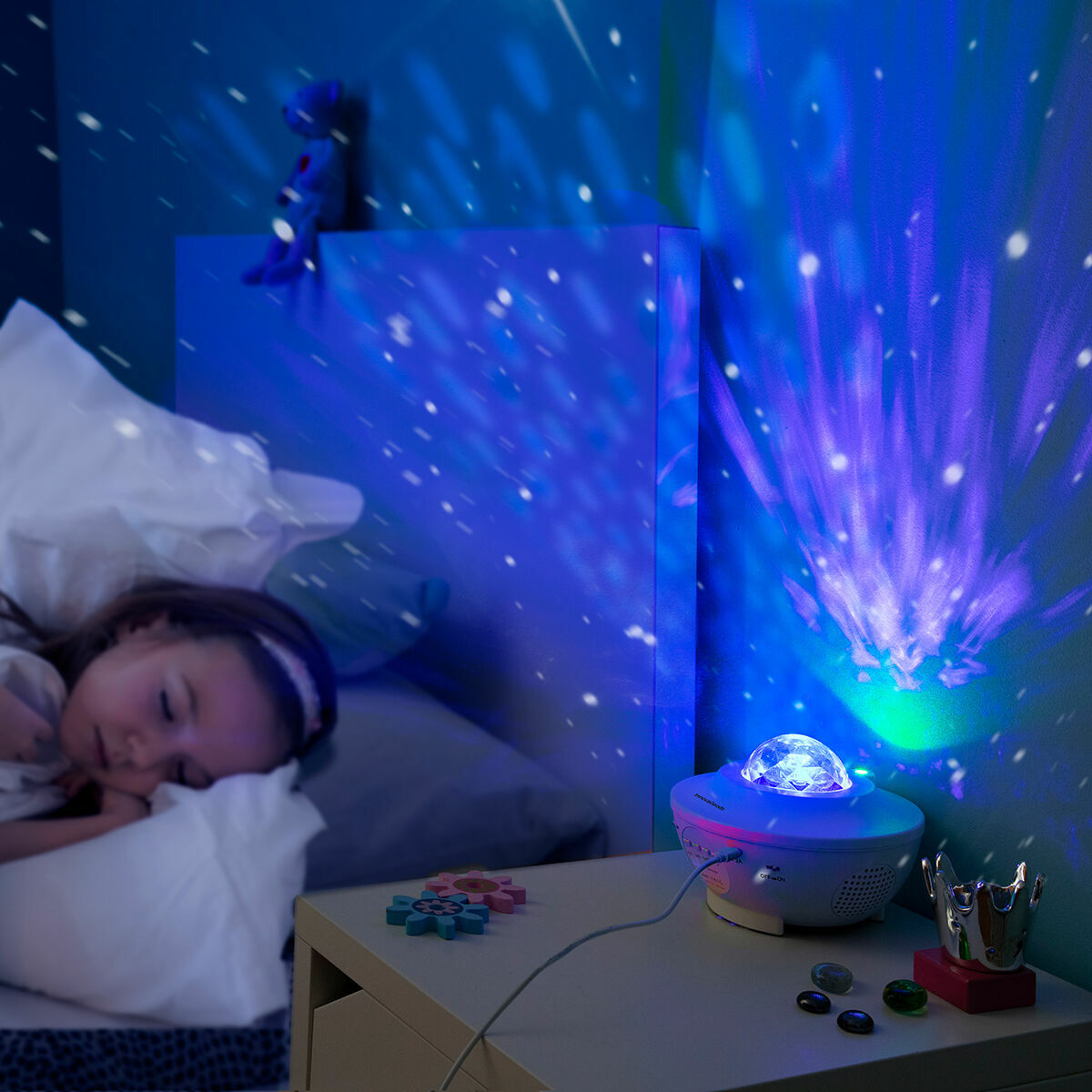 The projector is used as a night light, creating a calming blue starry effect in a bedroom. A child is asleep next to the projection, demonstrating its use for a peaceful sleep.