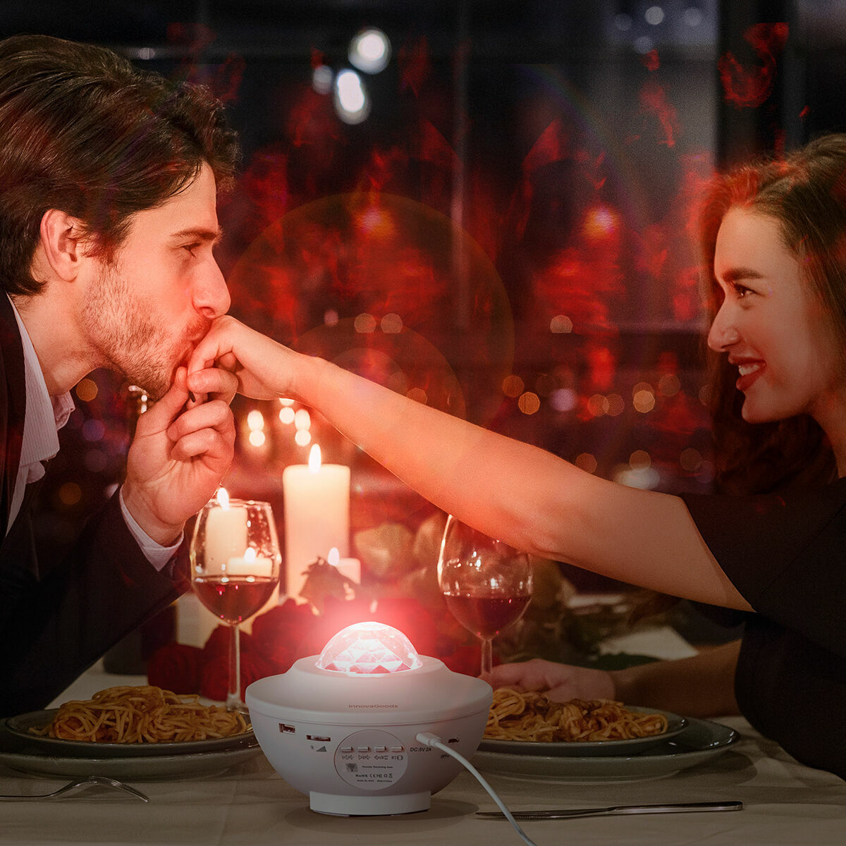 A romantic dinner setting with the projector creating a warm, red ambiance. Two people enjoy the atmosphere, with the projector enhancing the mood on the table.