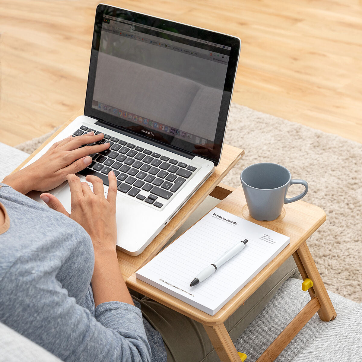 Woman sitting with the table on her lap, with a laptop and taking notes, set in a bright, well-furnished living space.