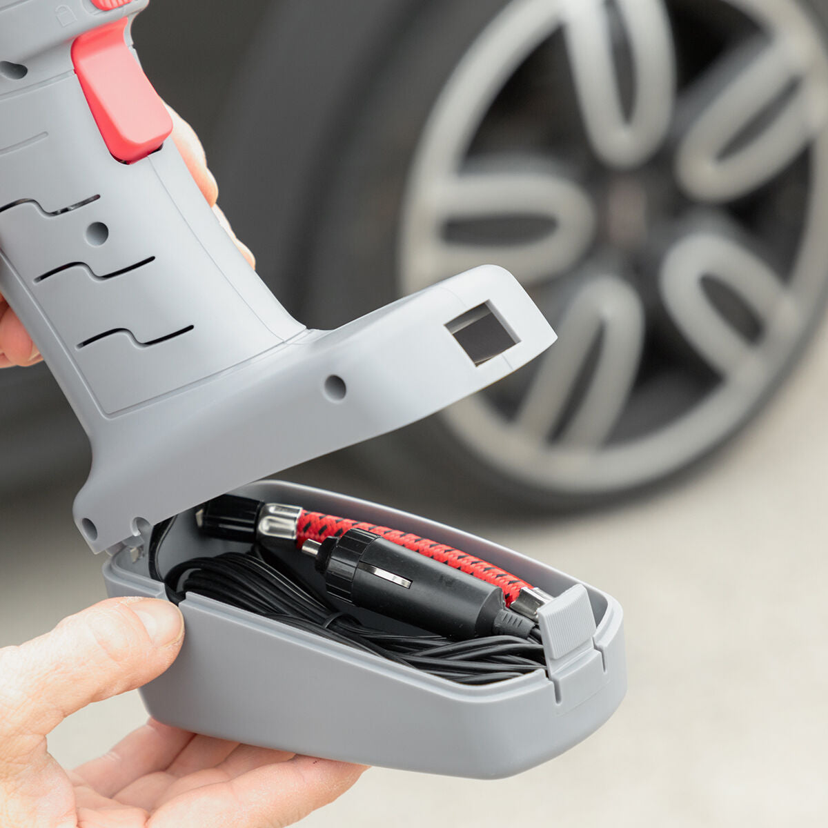 The base compartment of the air compressor open to reveal storage for its hose and power cable, showing its compact and efficient design.