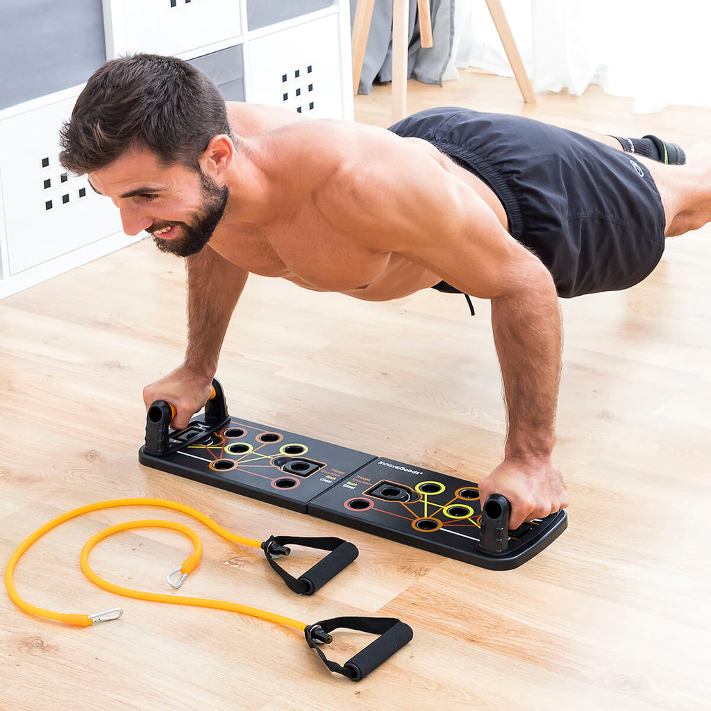 A person doing a push-up on the black push-up board, which has multiple colored slots and detachable handles. Bright orange resistance bands lie on the wooden floor.