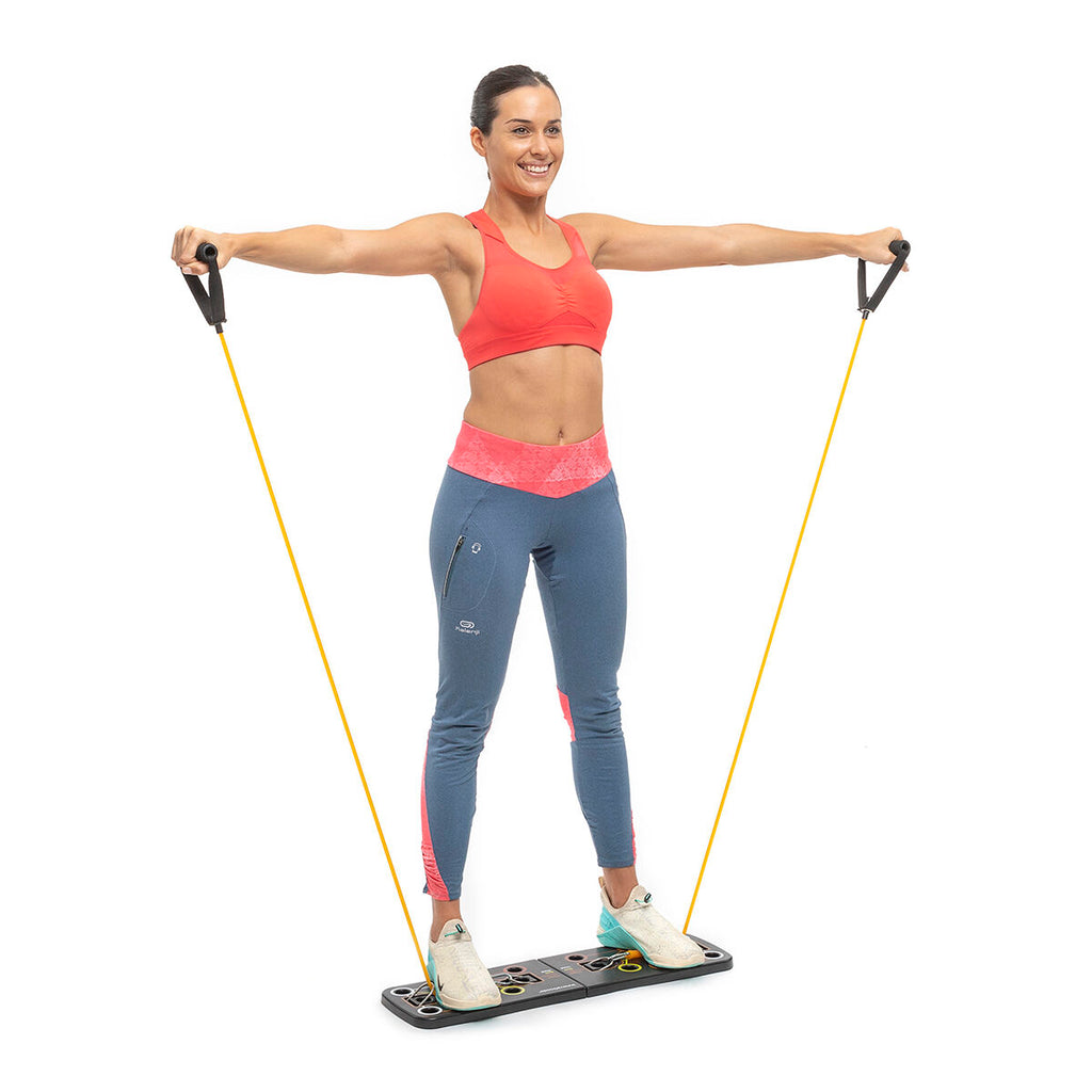 A person standing on the push-up board, performing a resistance band exercise with both arms extended outward.