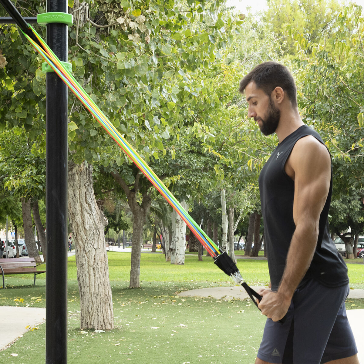 A male user doing an exercise with resistance bands outdoors in a park setting.
