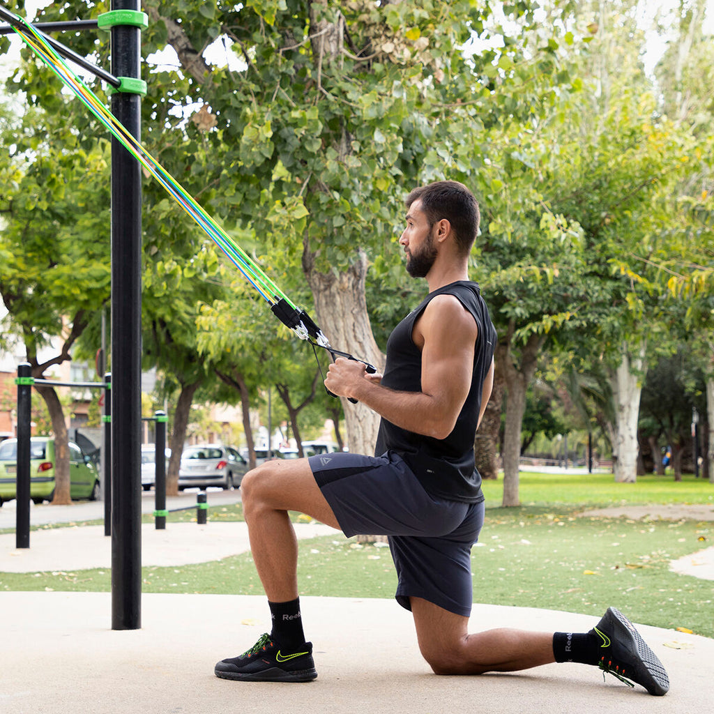 A male user kneeling while pulling resistance bands attached to a pole in a park setting.