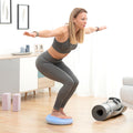 A woman in athletic wear using the balance cushion for squats in a home setting. The cushion is light blue with a textured surface.