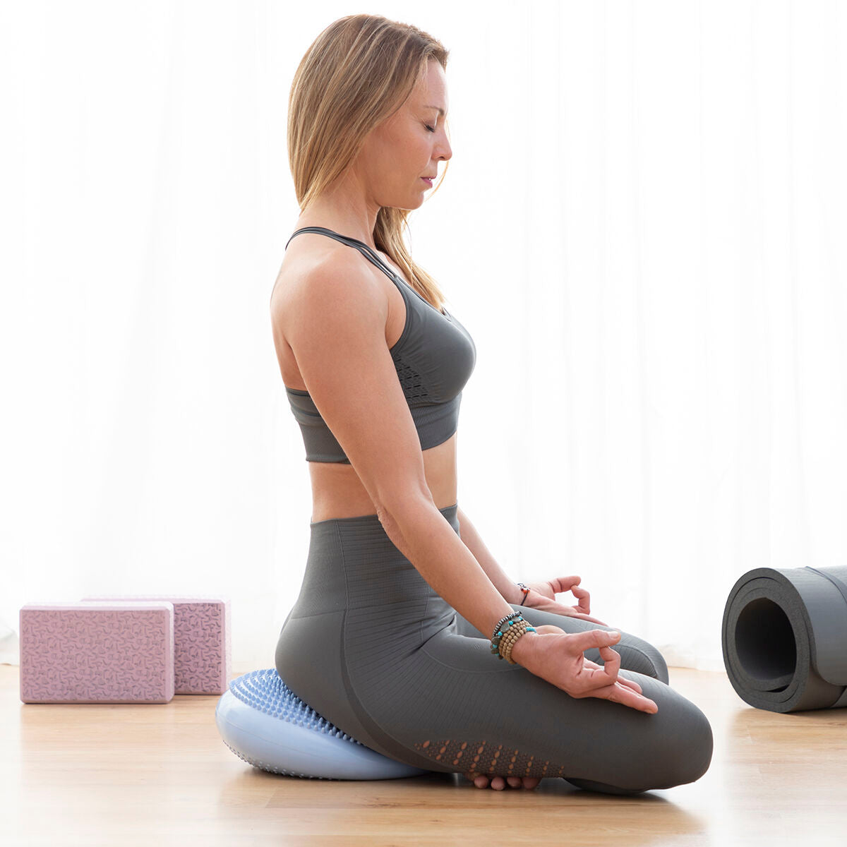 A woman practicing yoga by sitting in a meditation pose on the Cushport Balance Cushion, showcasing its use for relaxation and core engagement.