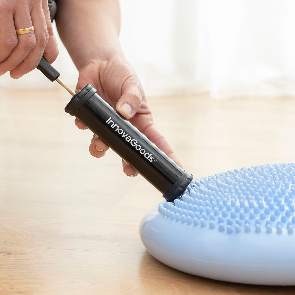 A close-up of hands using the black InnovaGoods pump to inflate the light blue balance cushion.