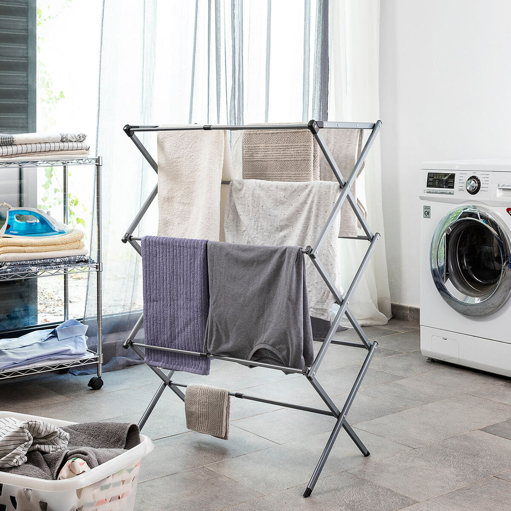 A metal clothes dryer standing in a laundry room. The dryer is open with clothes hanging on it, placed beside a washing machine. The floor and subtle window light add to the context.