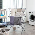 A metal clothes dryer standing in a laundry room. The dryer is open with clothes hanging on it, placed beside a washing machine. The floor and subtle window light add to the context.