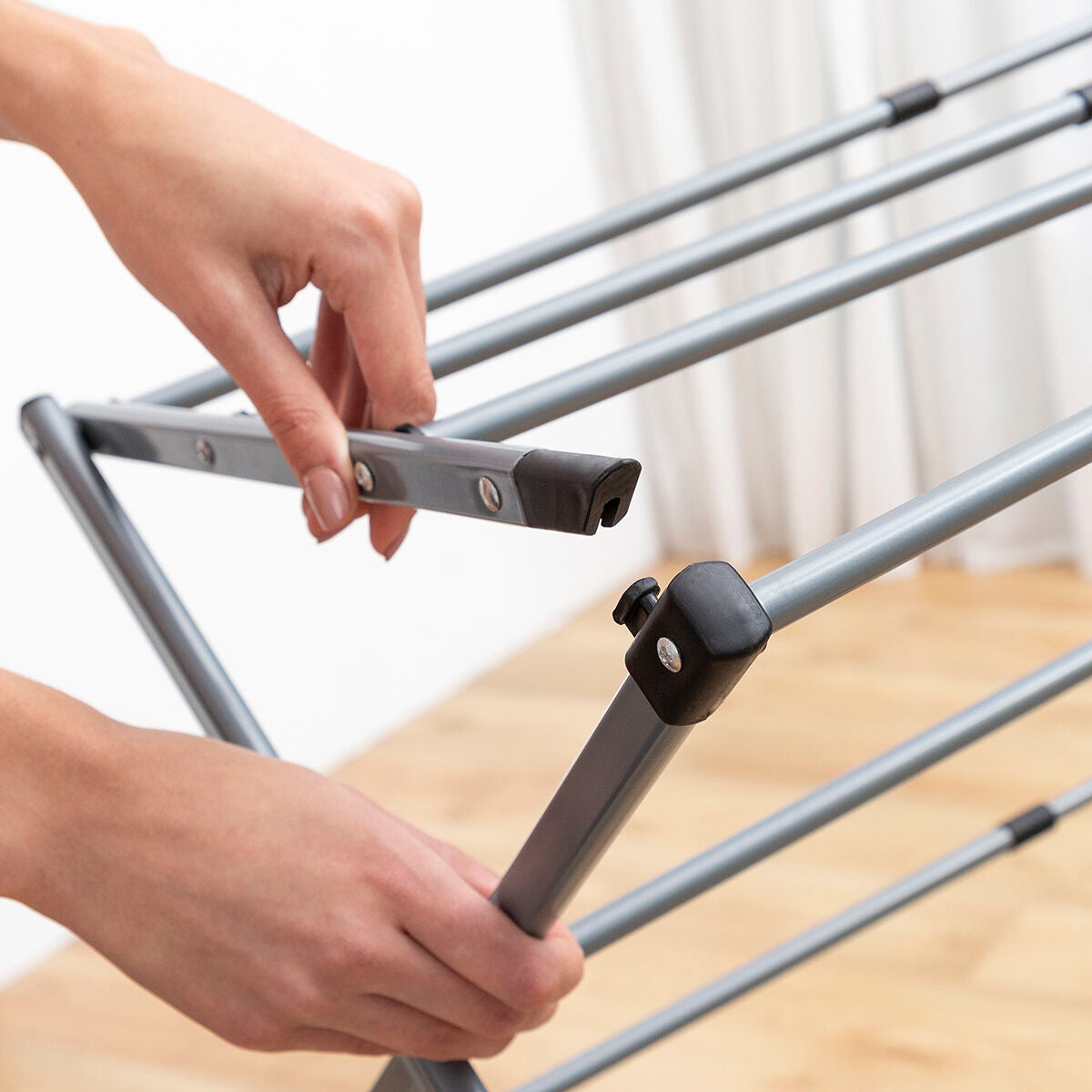 Close-up of a hand adjusting the metal clothes dryer's frame, focusing on its simple assembly and folding mechanism.