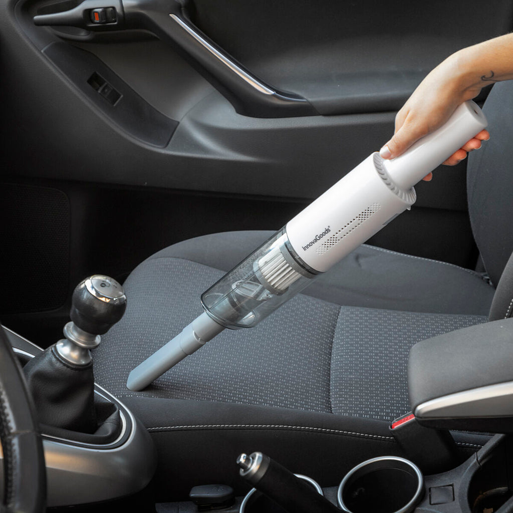 A person uses the handheld vacuum to clean the interior of a car, focusing on the seat surfaces. The white and gray vacuum design meshes well with the vehicle's interior, suggesting its suitability for car cleaning.