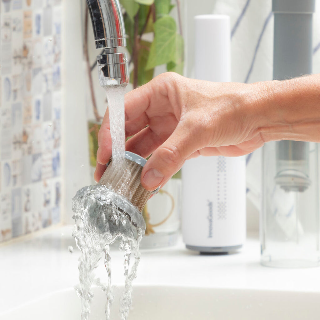 A filter from the vacuum is being rinsed under a running tap. This image highlights the easy maintenance of the product, with the main vacuum body visible in the blurred background.