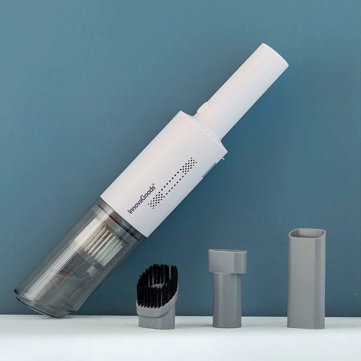 The vacuum is displayed with its accessories on a blue background. The white vacuum cleaner, along with a few gray attachments laid out, gives a clear view of the product elements and emphasizes its compact and organized storage potential.