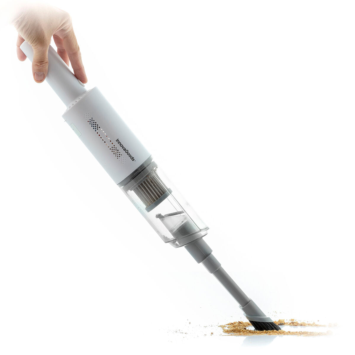 A hand is seen holding the vacuum cleaner picking up crumbs from a surface. The vacuum's compact design is highlighted with its transparent dust compartment allowing for easy visibility of collected debris. There's a sense of action as crumbs are visibly being sucked up.