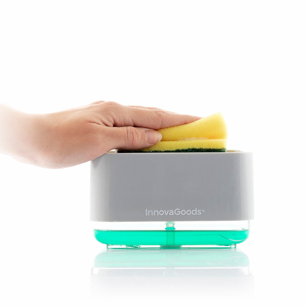 A lifestyle image showing a hand pressing a sponge onto the InnovaGoods Pushoap 2-in-1 Soap Dispenser, dispensing green soap. The scene is set against a white background, highlighting the product's functionality.