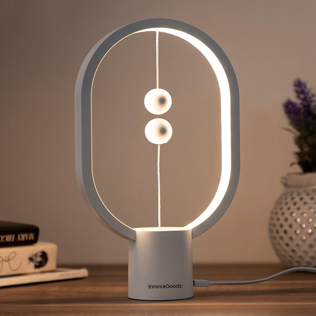 Detail view of the InnovaGoods Balance Lamp on a wooden table, highlighting the magnetic switch mechanism with books and decorations providing an additional context.