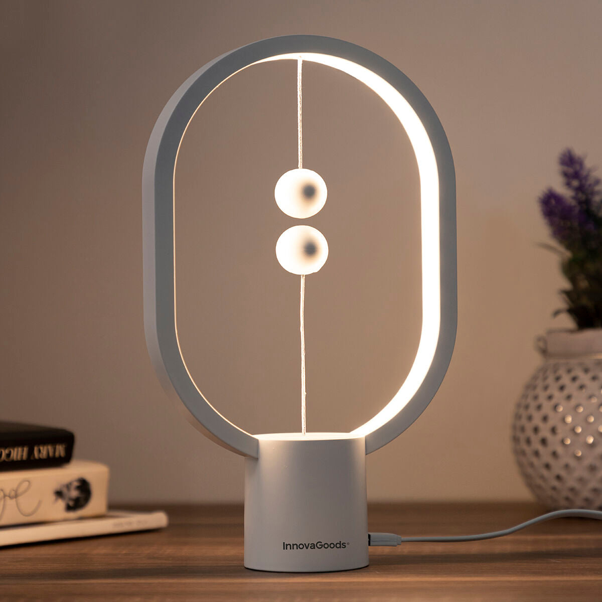 Detail view of the InnovaGoods Balance Lamp on a wooden table, highlighting the magnetic switch mechanism with books and decorations providing an additional context.