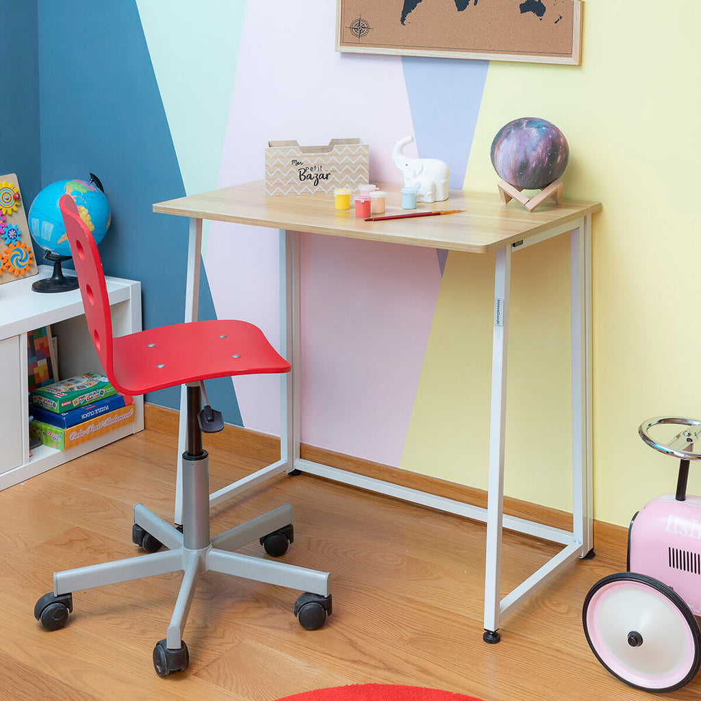A desk placed in a colorful children's room next to a red chair, demonstrating the desk's versatility.