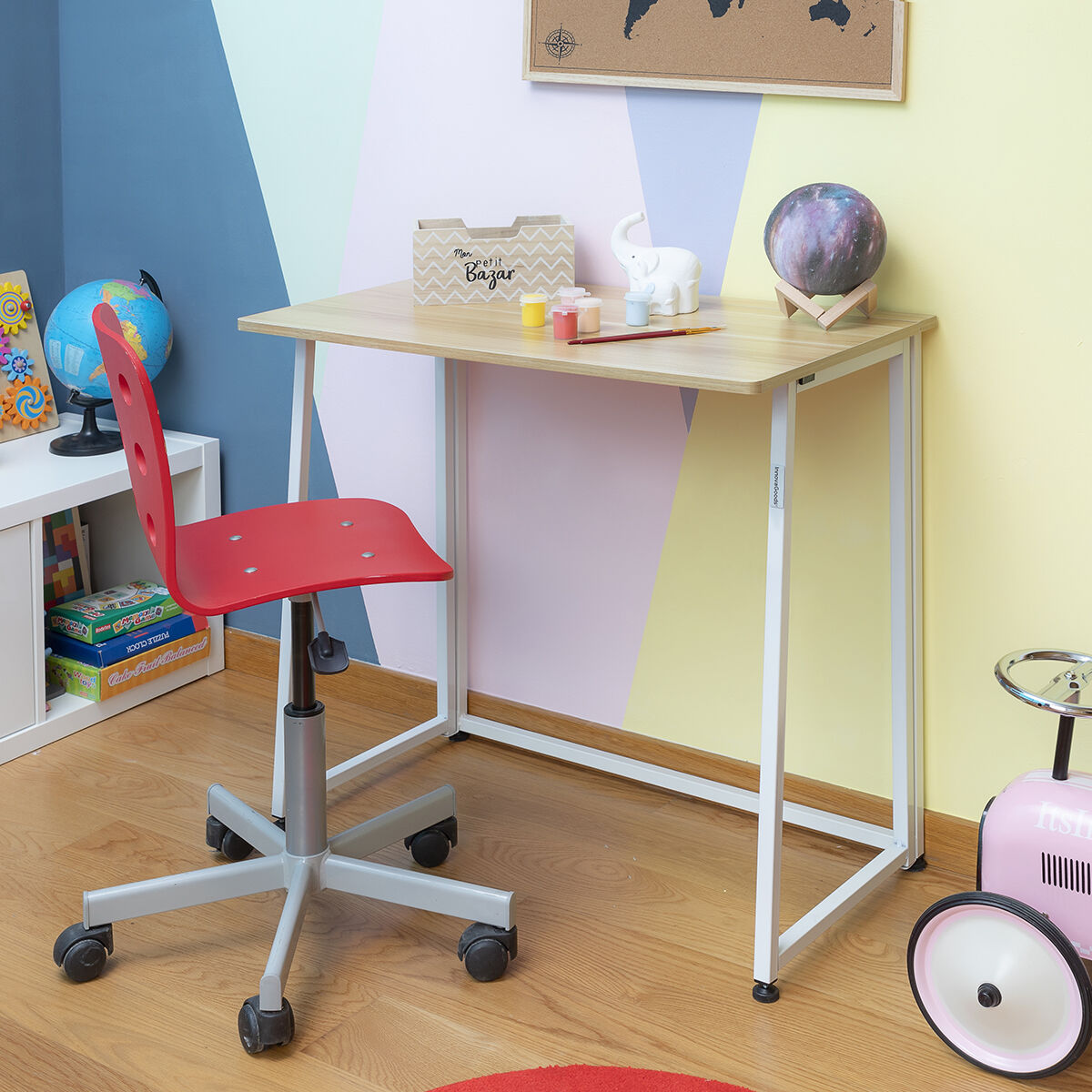 A desk placed in a colorful children's room next to a red chair, demonstrating the desk's versatility.