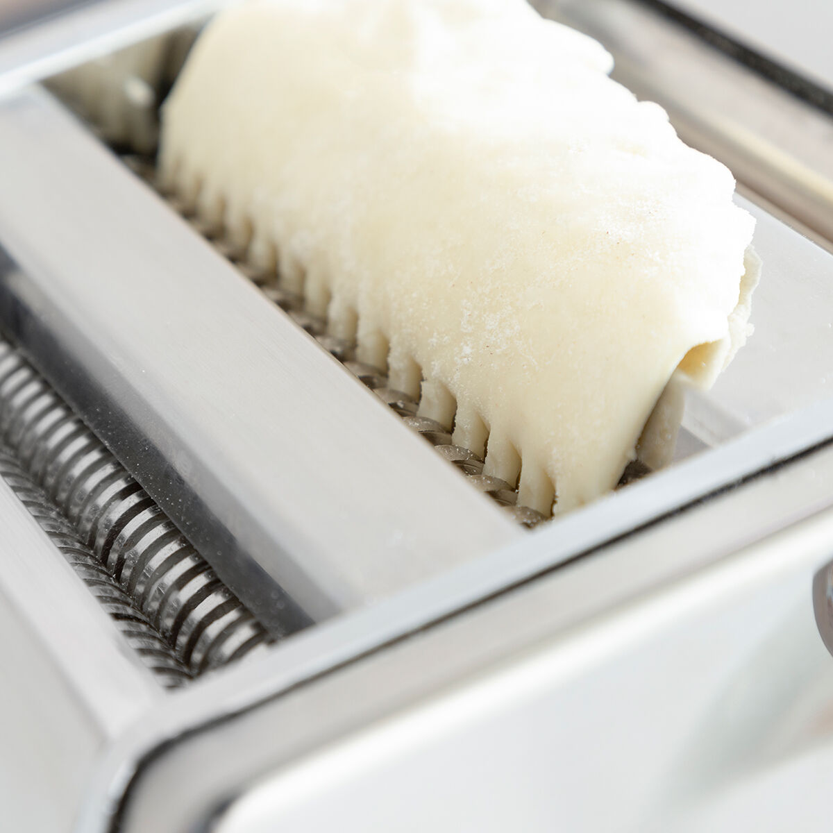 Close-up of dough being processed in the cutting section of the pasta maker, exhibiting the tool's efficiency.