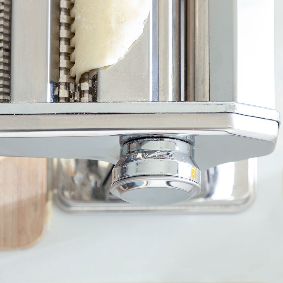 Close-up detail of the pasta maker's rollers and a partial dough in the machine, showing texture and construction of the tool.