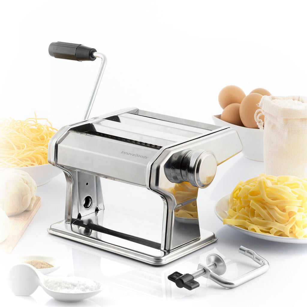 The pasta maker placed on a table with pasta and flour ingredients around it. The setting is bright and includes bowls of noodles and eggs, indicating preparation.
