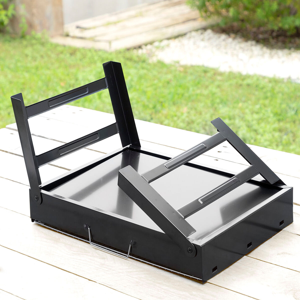 The grill shown folded with legs extended on a wooden surface, demonstrating portability.