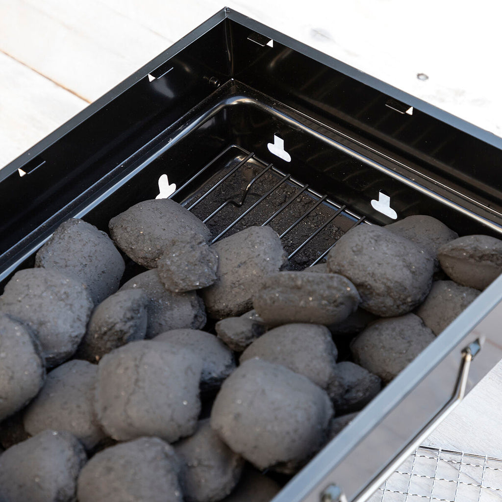 The interior of the portable grill filled with charcoal, preparing for use.